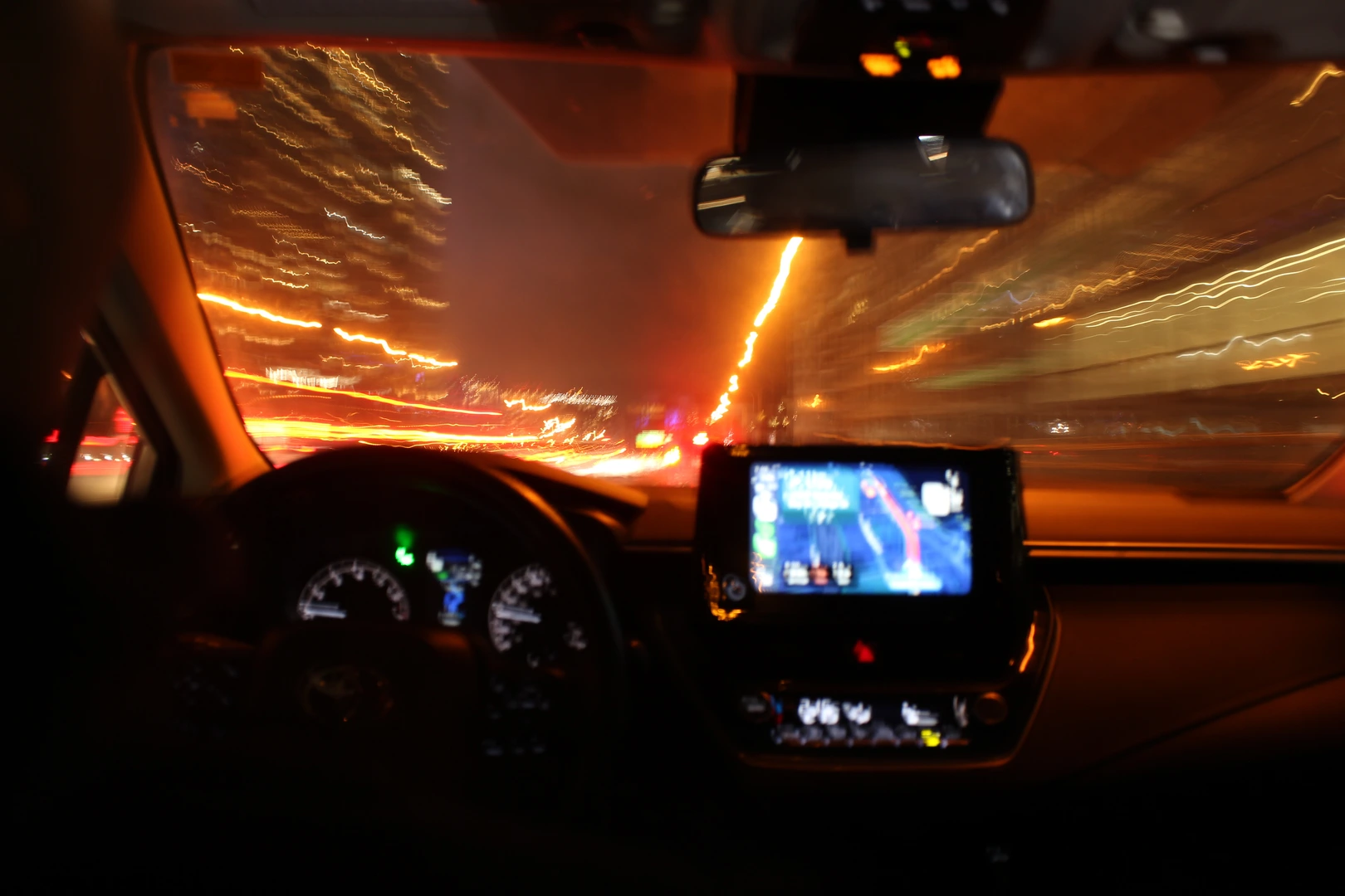 A blurred night drive from the driver's seat, oncoming lights smeared across the windshield.