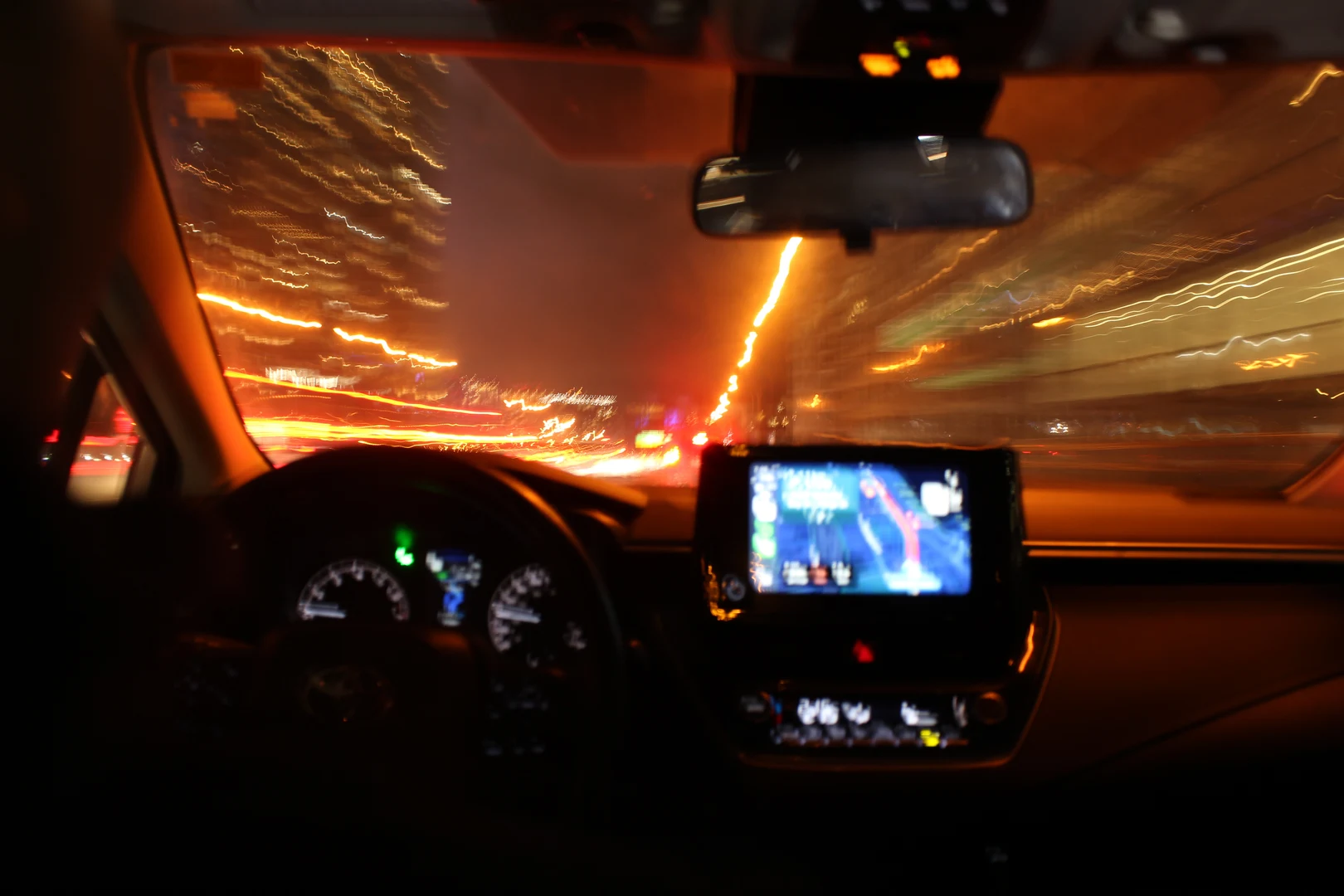 A blurred night drive from the driver's seat, oncoming lights smeared across the windshield.