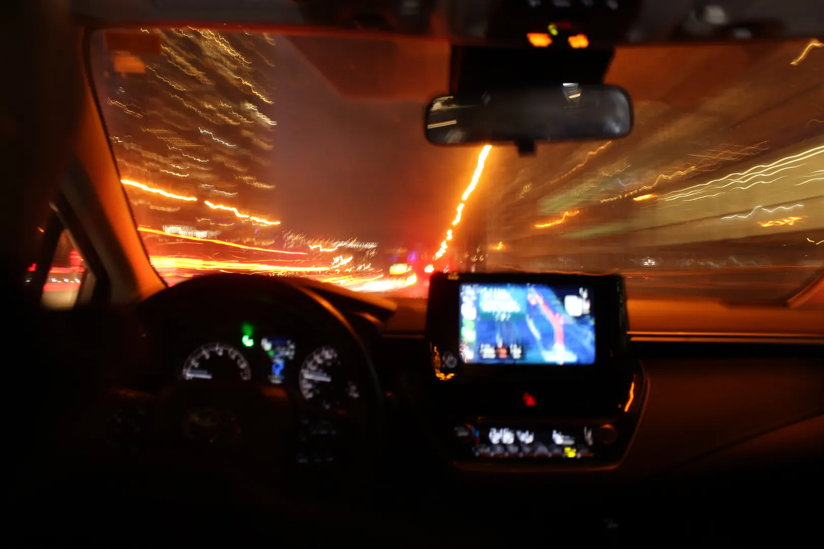 A blurred night drive from the driver's seat, oncoming lights smeared across the windshield.