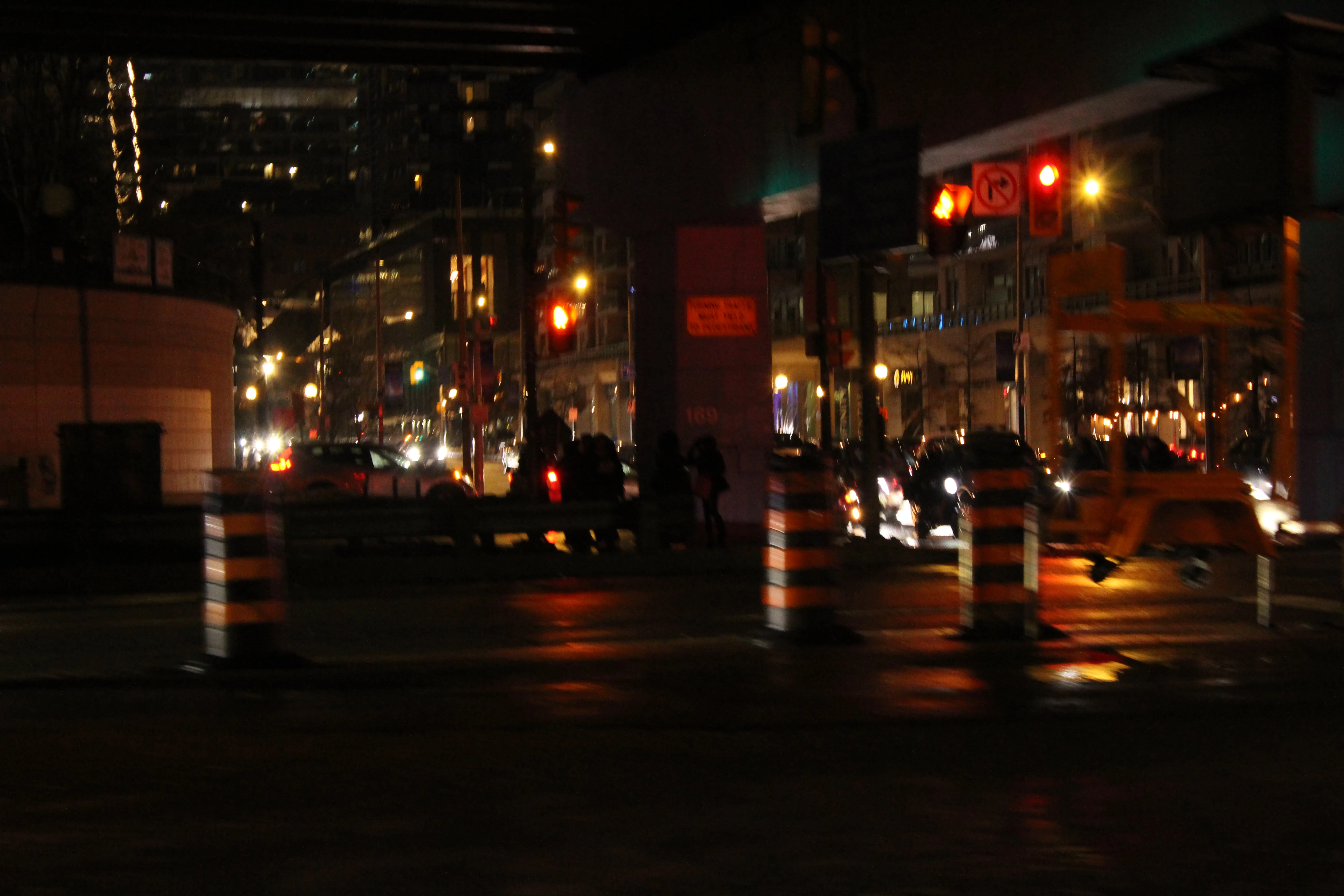 A wet city street at night, traffic cones in the foreground and red signals reflecting on the asphalt.
