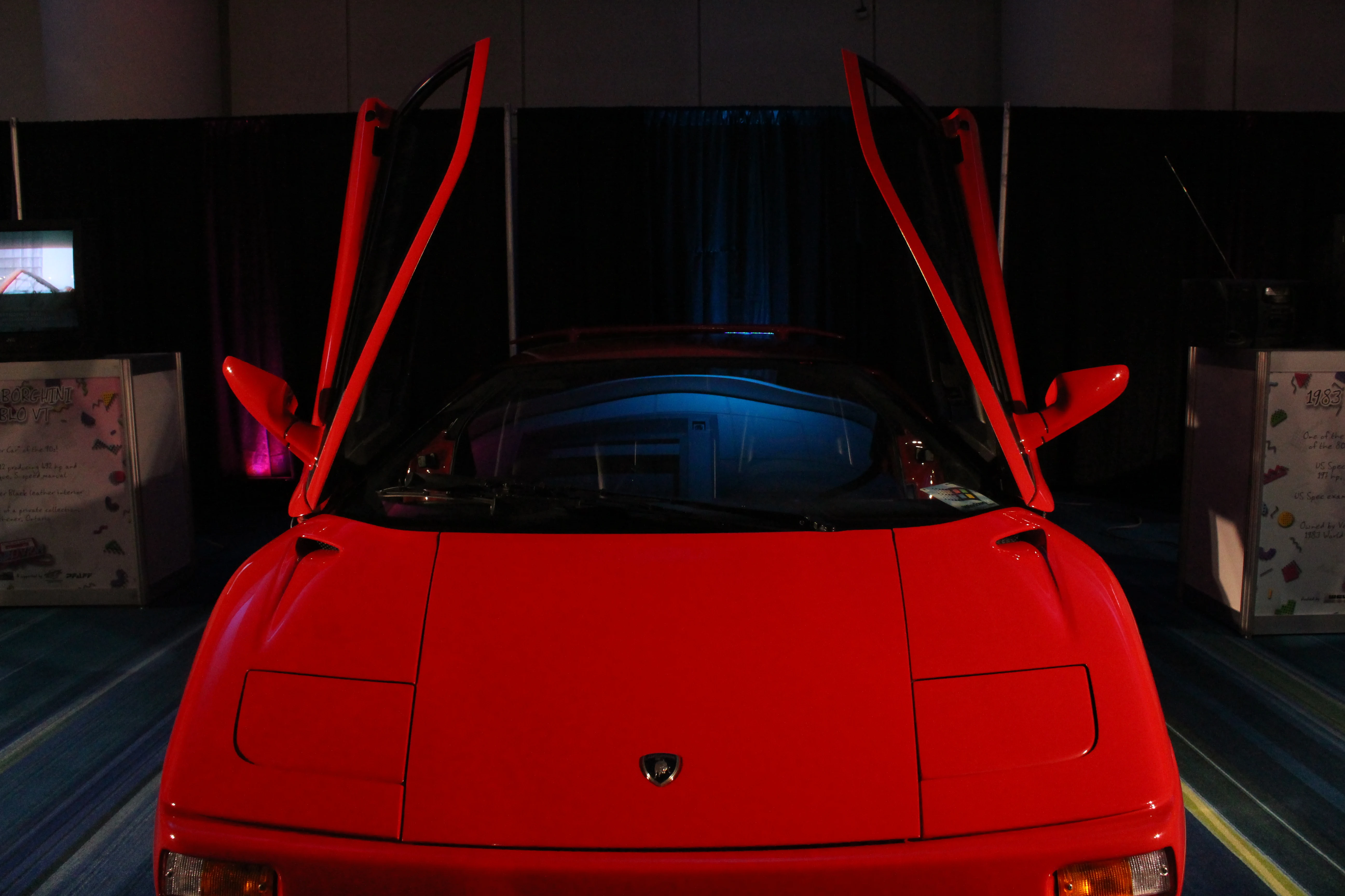 A red 1990s Lamborghini Diablo VT photographed head-on with both scissor doors raised in a dim exhibition hall.
