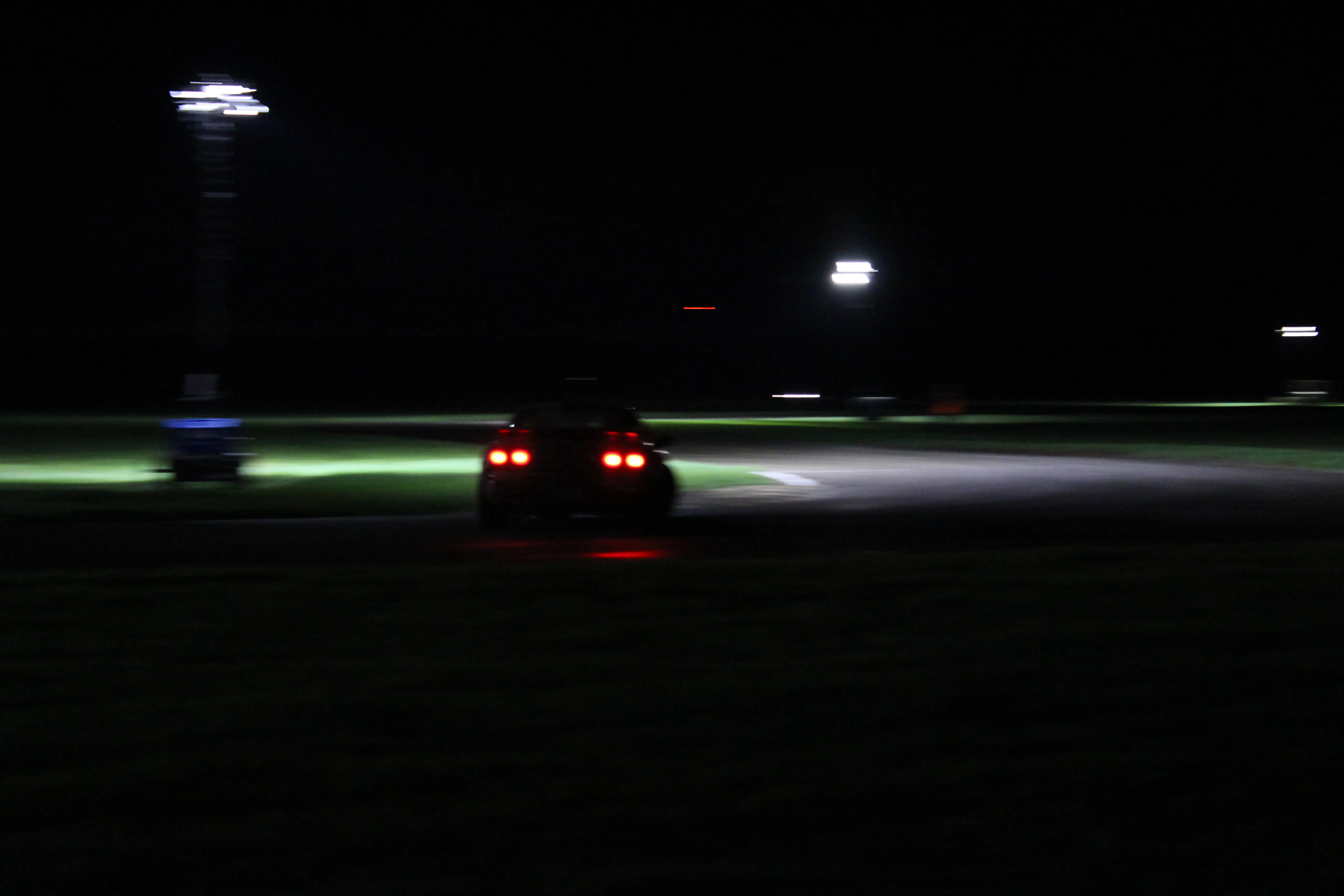A car blurring through a corner at night, taillights streaking under distant track lighting.