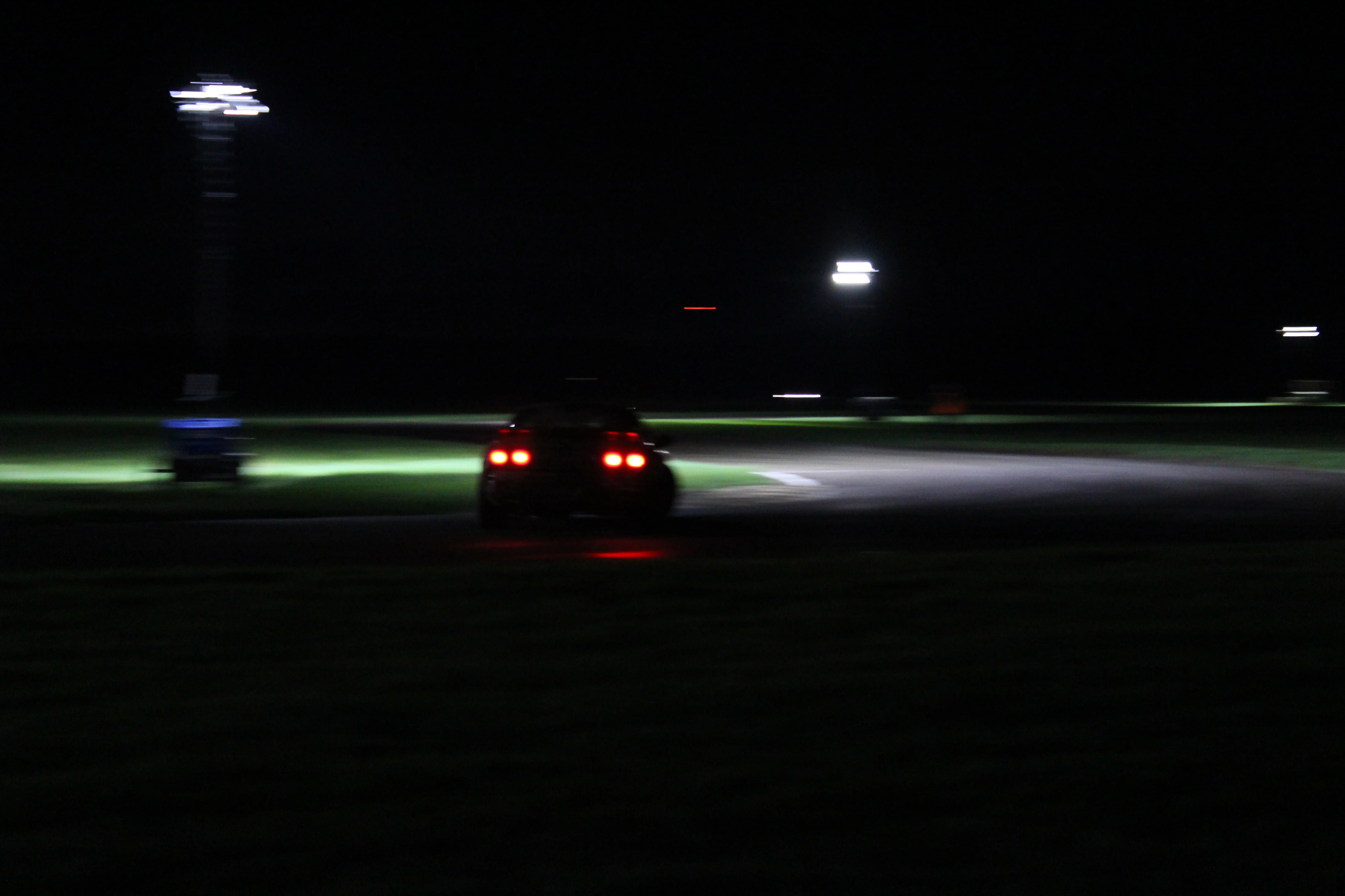 A car blurring through a corner at night, taillights streaking under distant track lighting.