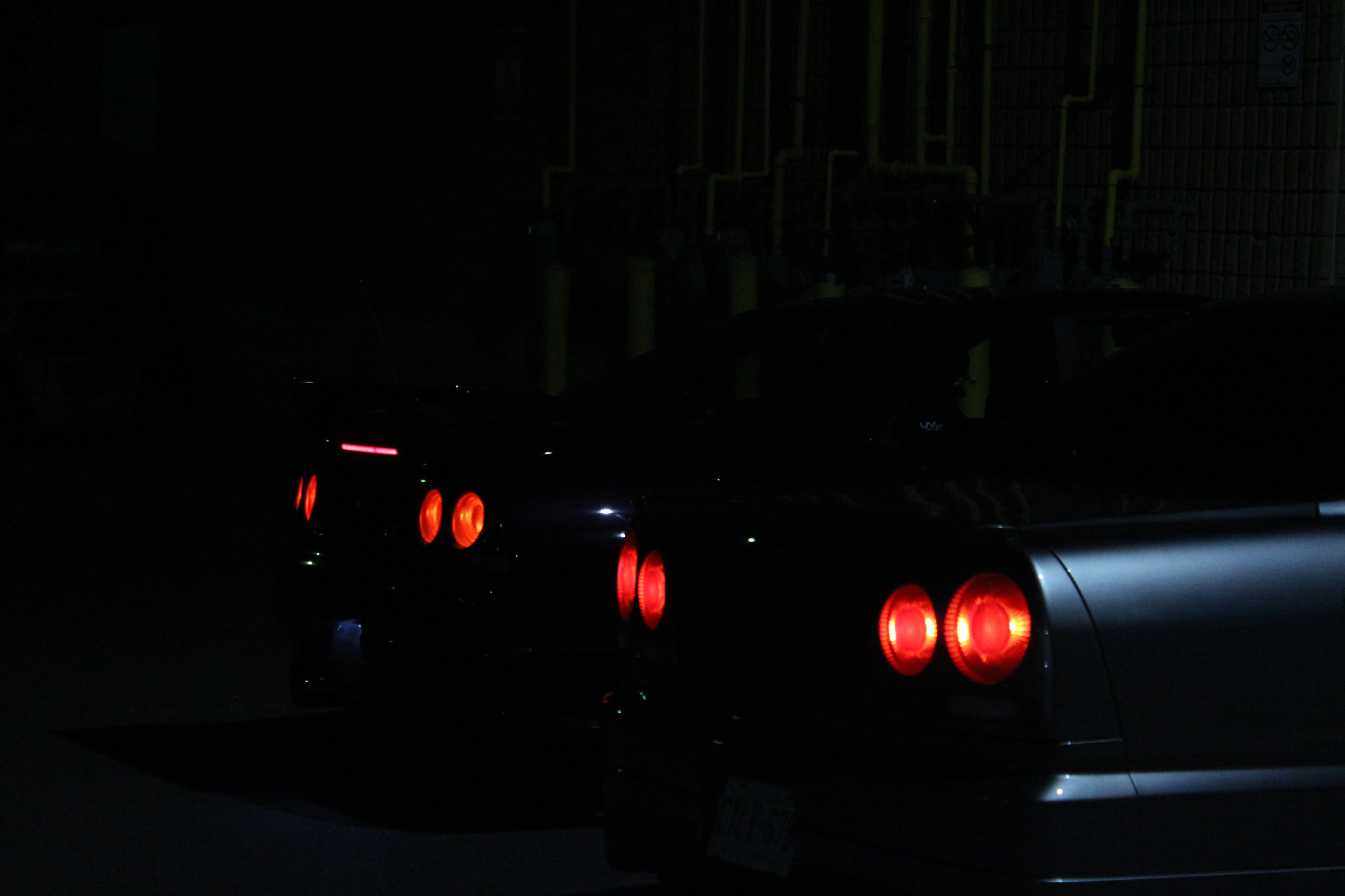 The round taillights of two Nissan Skyline GT-Rs glowing red in a dark lot.