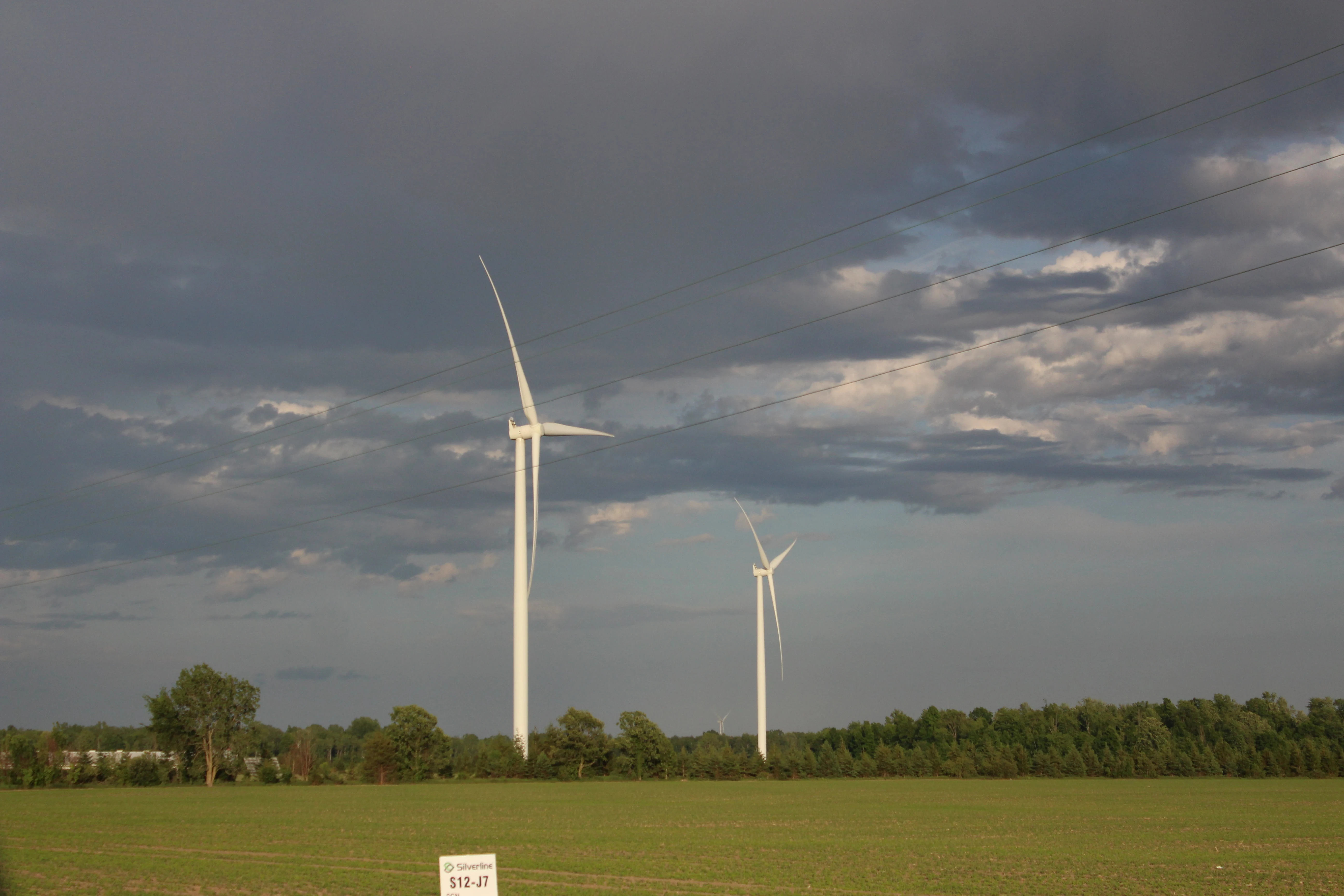 Two wind turbines rising over a green field under a bruised, stormy sky.