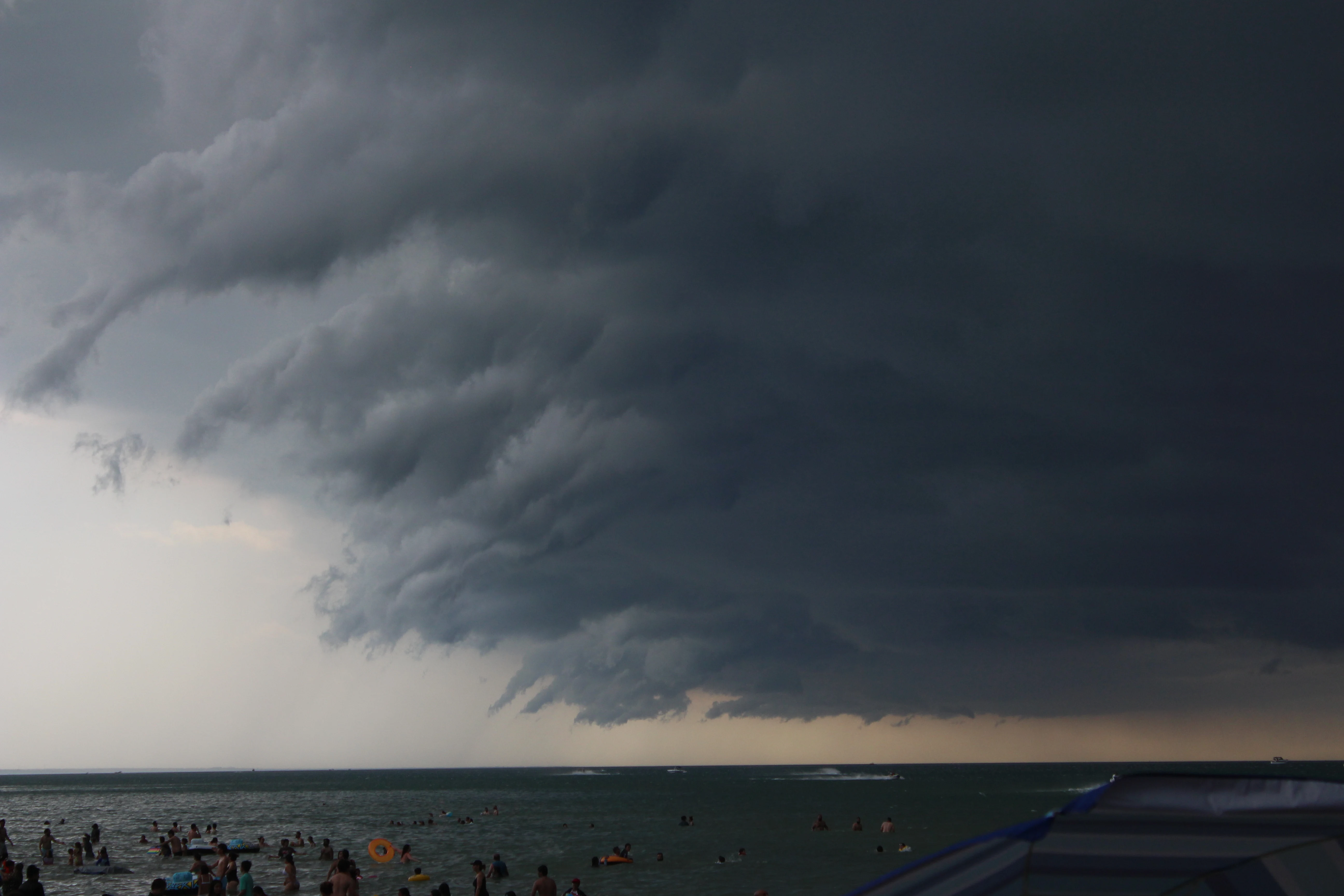 A dark storm front rolling in over a crowded beach, swimmers still in the water below.