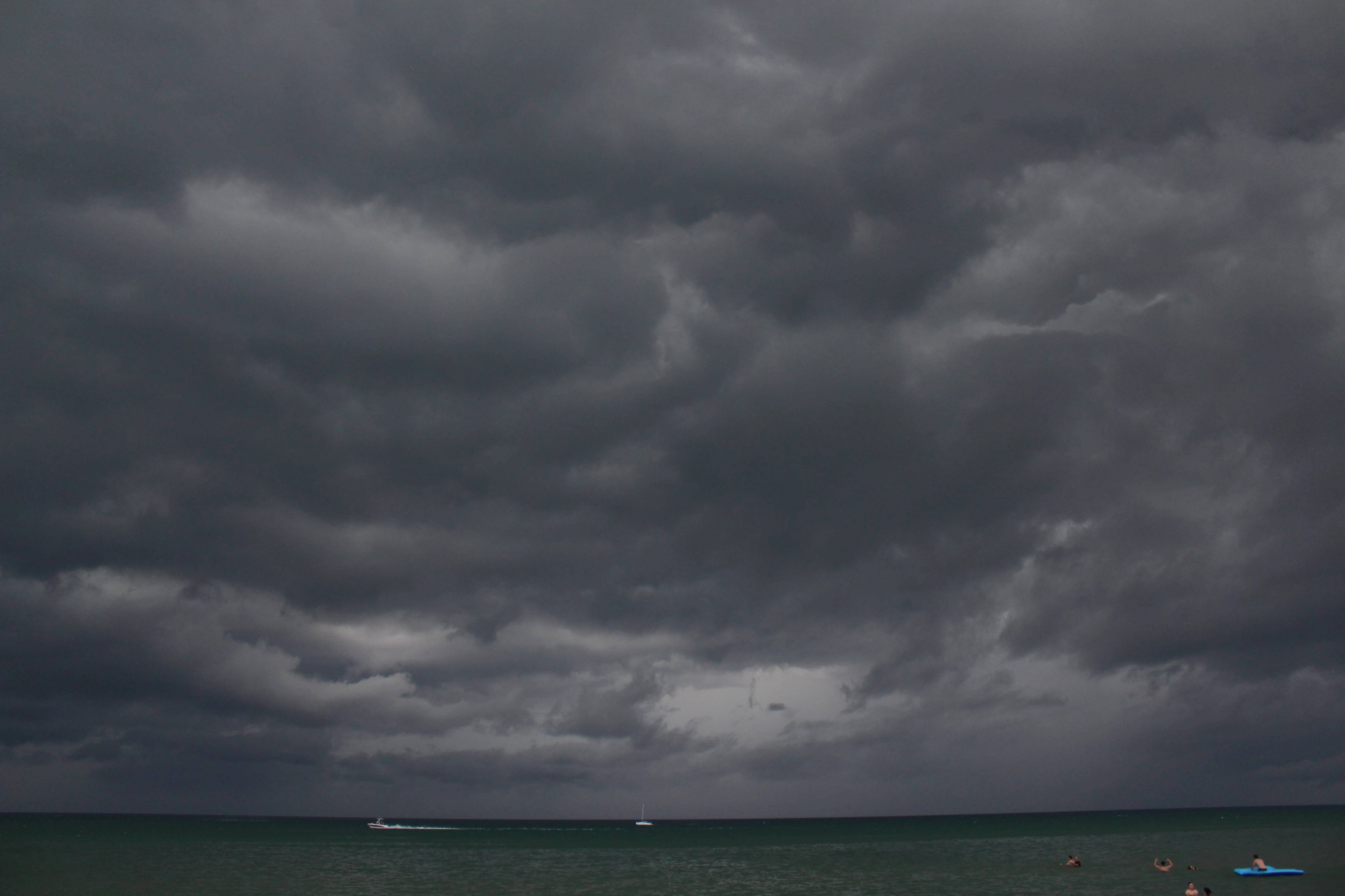 Heavy storm clouds massing over the lake with a lone sailboat and a speedboat on the water.