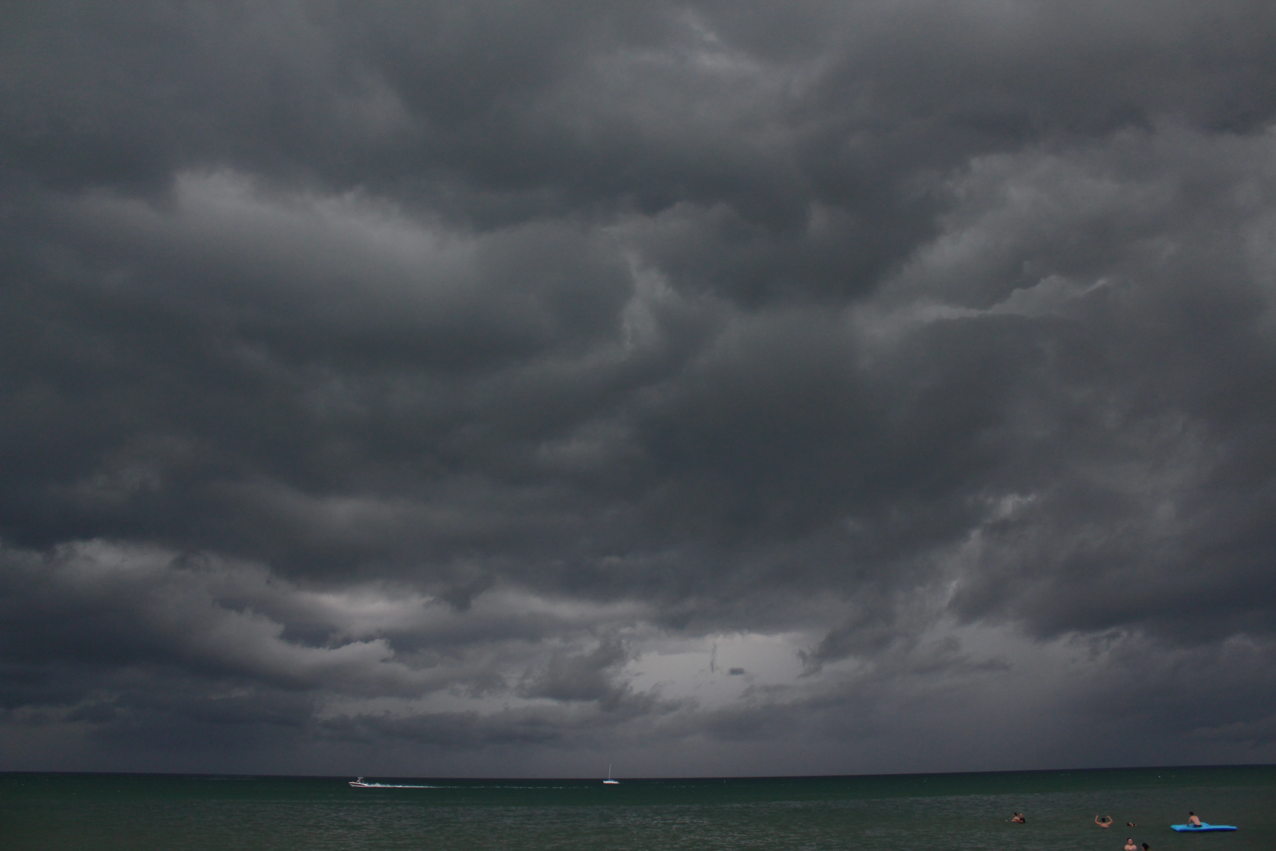 Heavy storm clouds massing over the lake with a lone sailboat and a speedboat on the water.