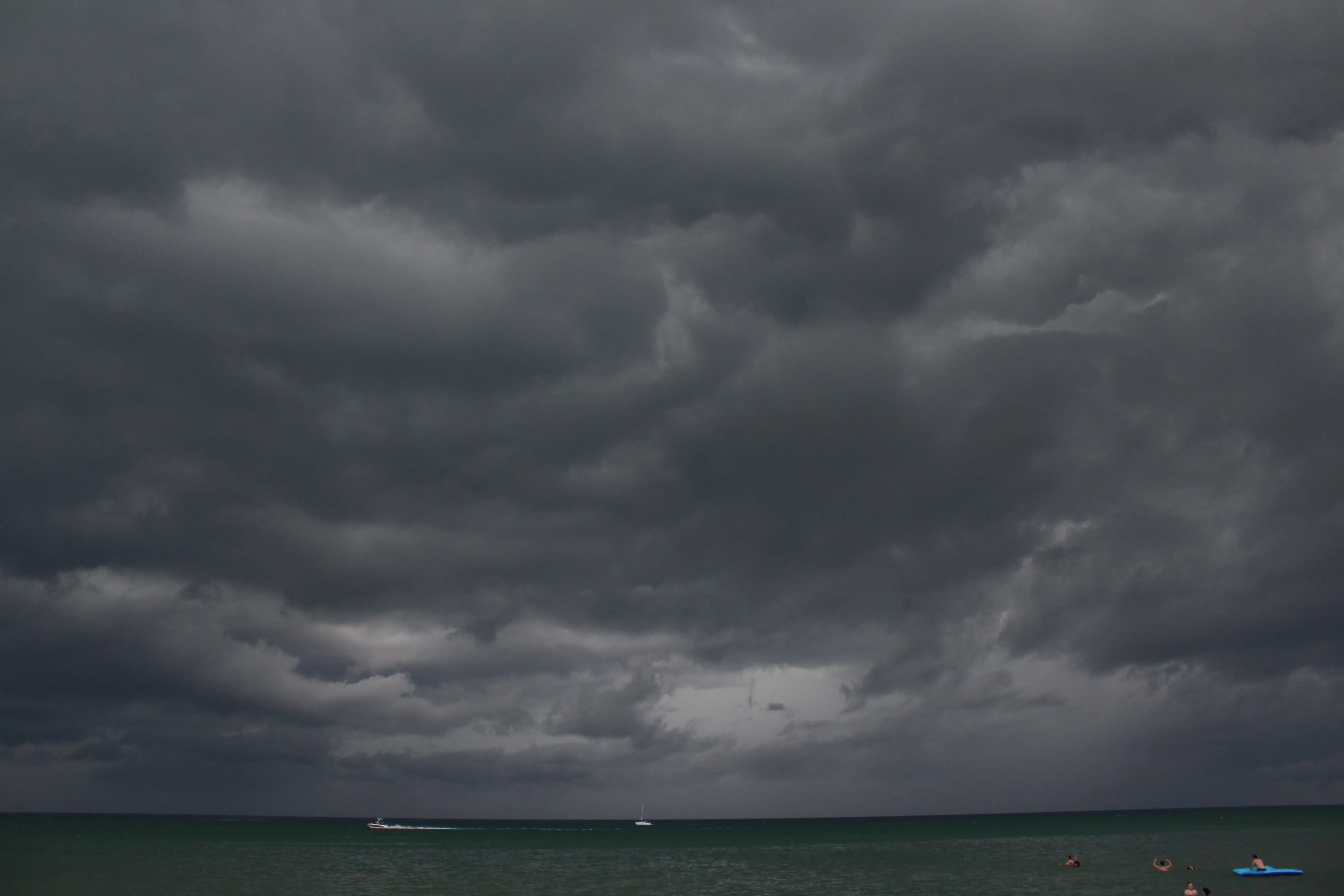 Heavy storm clouds massing over the lake with a lone sailboat and a speedboat on the water.