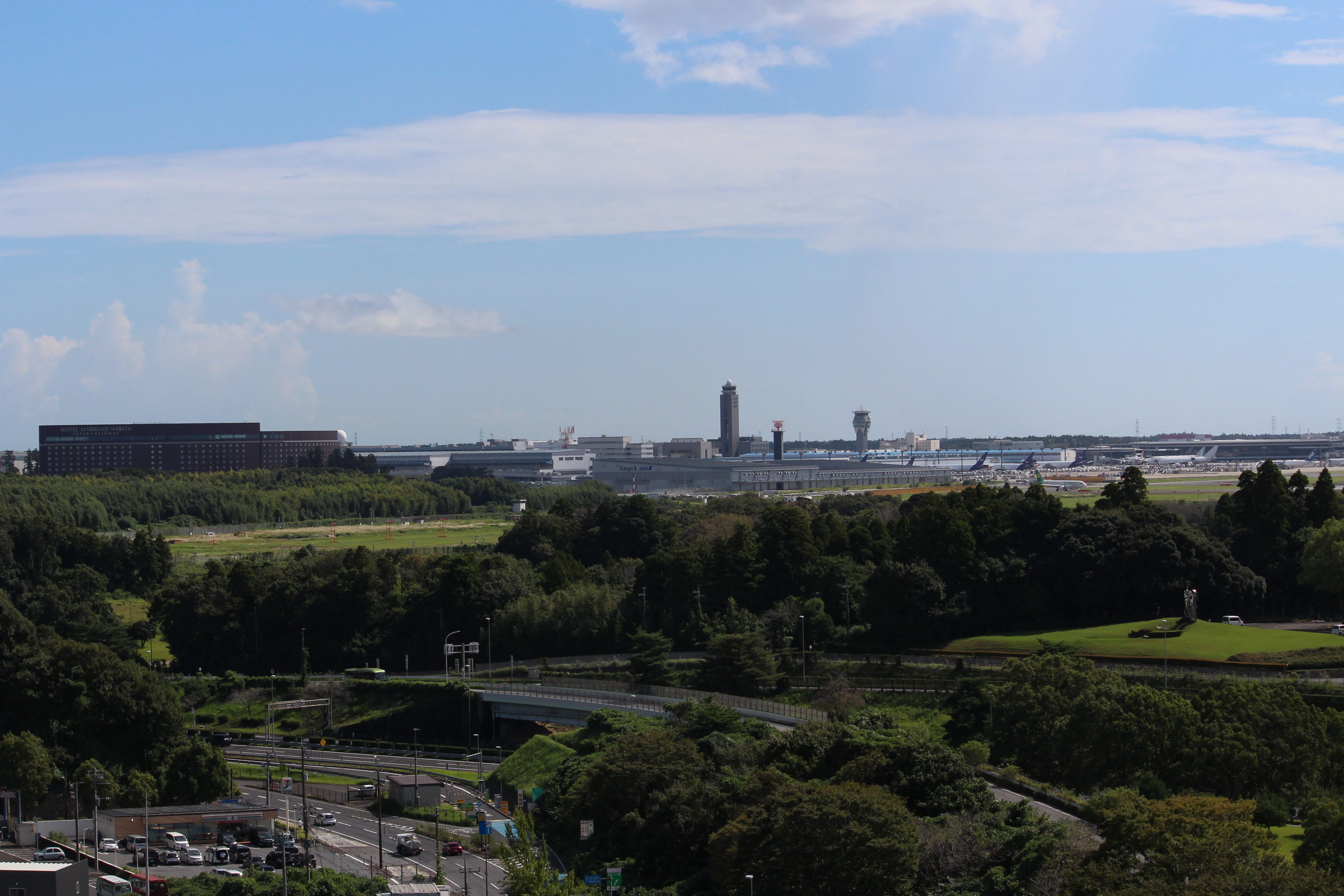 Distant airport terminal and control tower beyond an expanse of green field, seen from elevation.