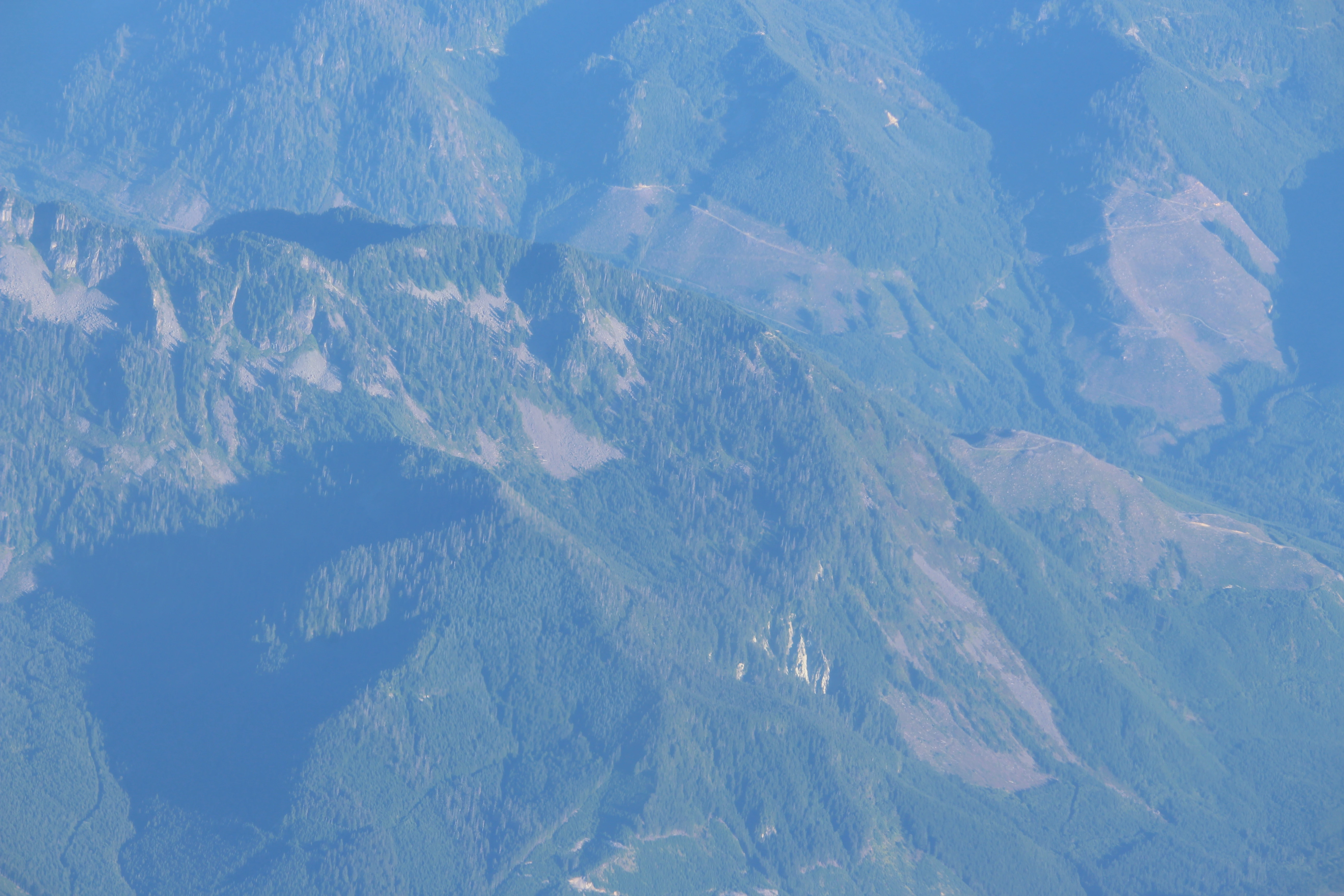 Forested mountain ridges seen from a plane window, folding away into blue haze far below.