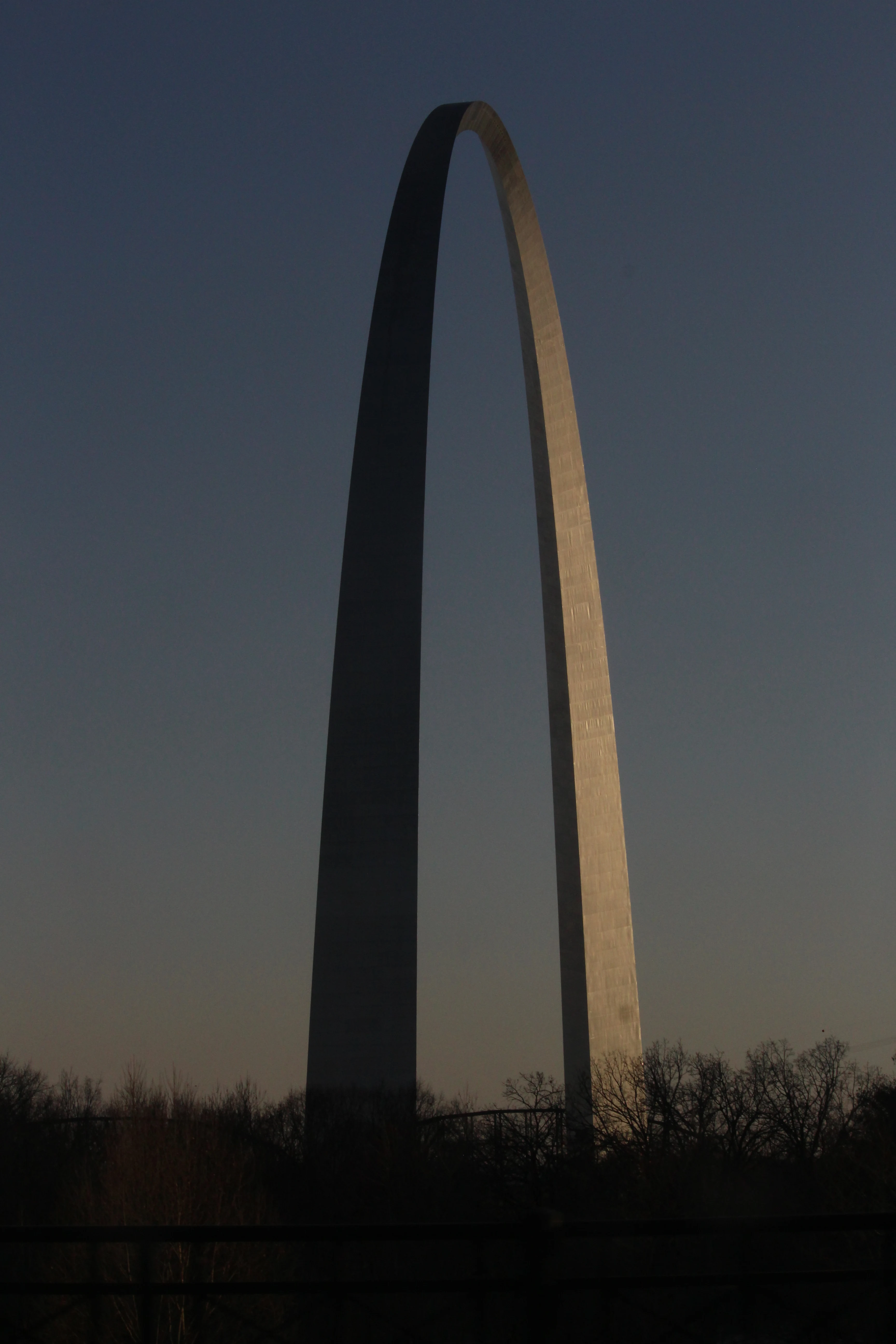 The Gateway Arch in St. Louis silhouetted at dusk, the catenary catching the last sun along its inner curve.