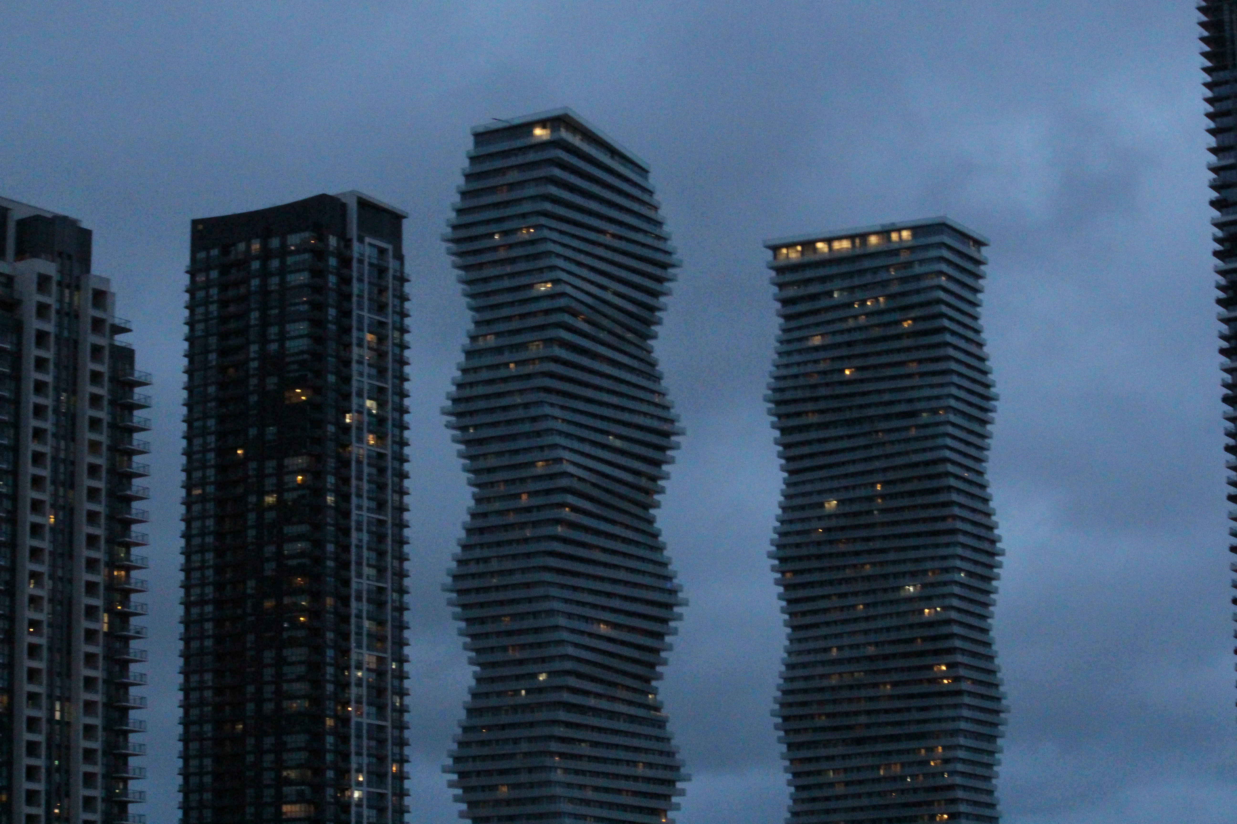 Two curved twisting residential towers against a flat overcast sky, slab balconies wrapping in a slow spiral.