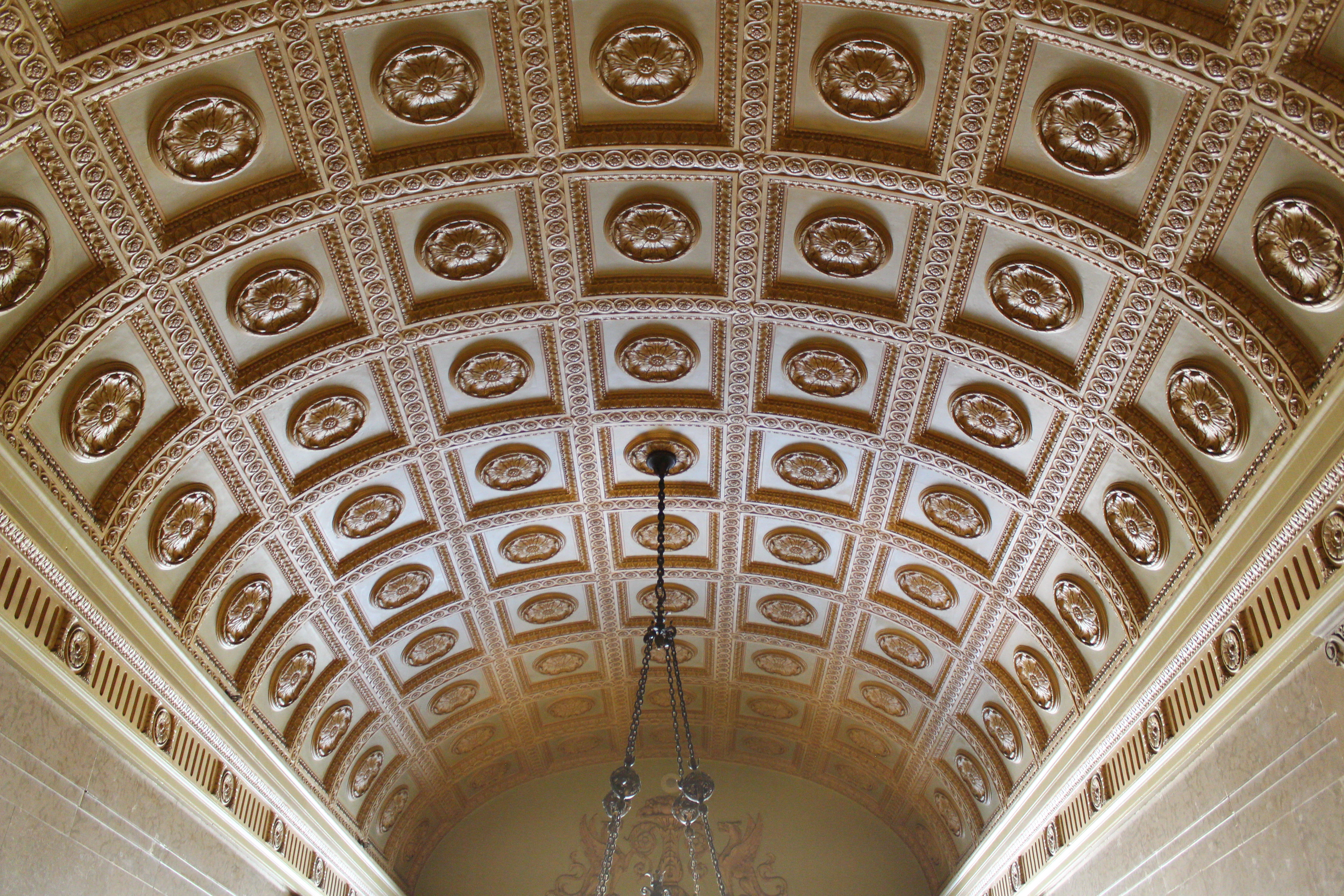 Coffered barrel-vault ceiling viewed from below, with a chandelier silhouetted against the rosettes.