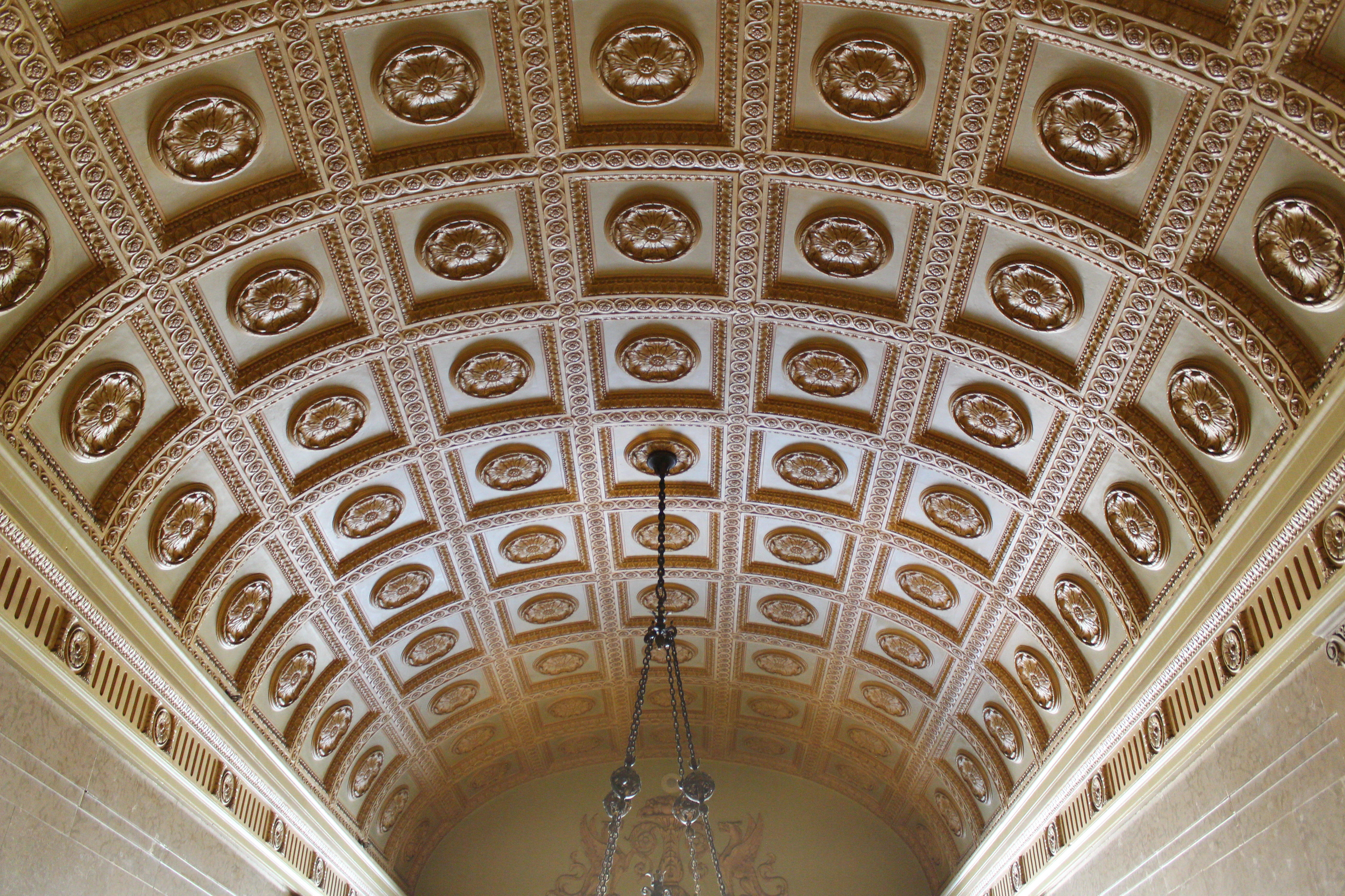 Coffered barrel-vault ceiling viewed from below, with a chandelier silhouetted against the rosettes.