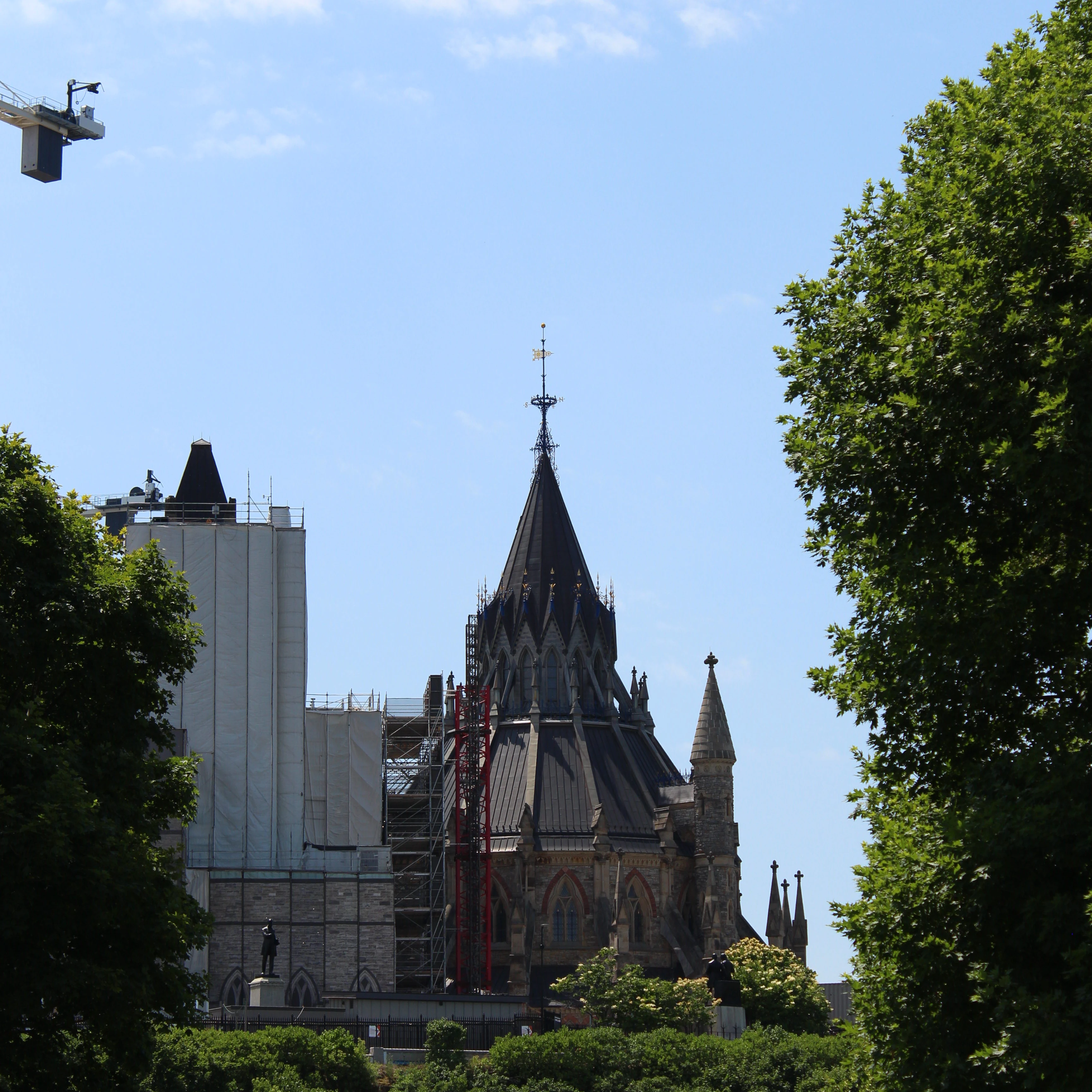 A single gothic spire of Notre Dame Basilica seen between trees against a clear summer sky.