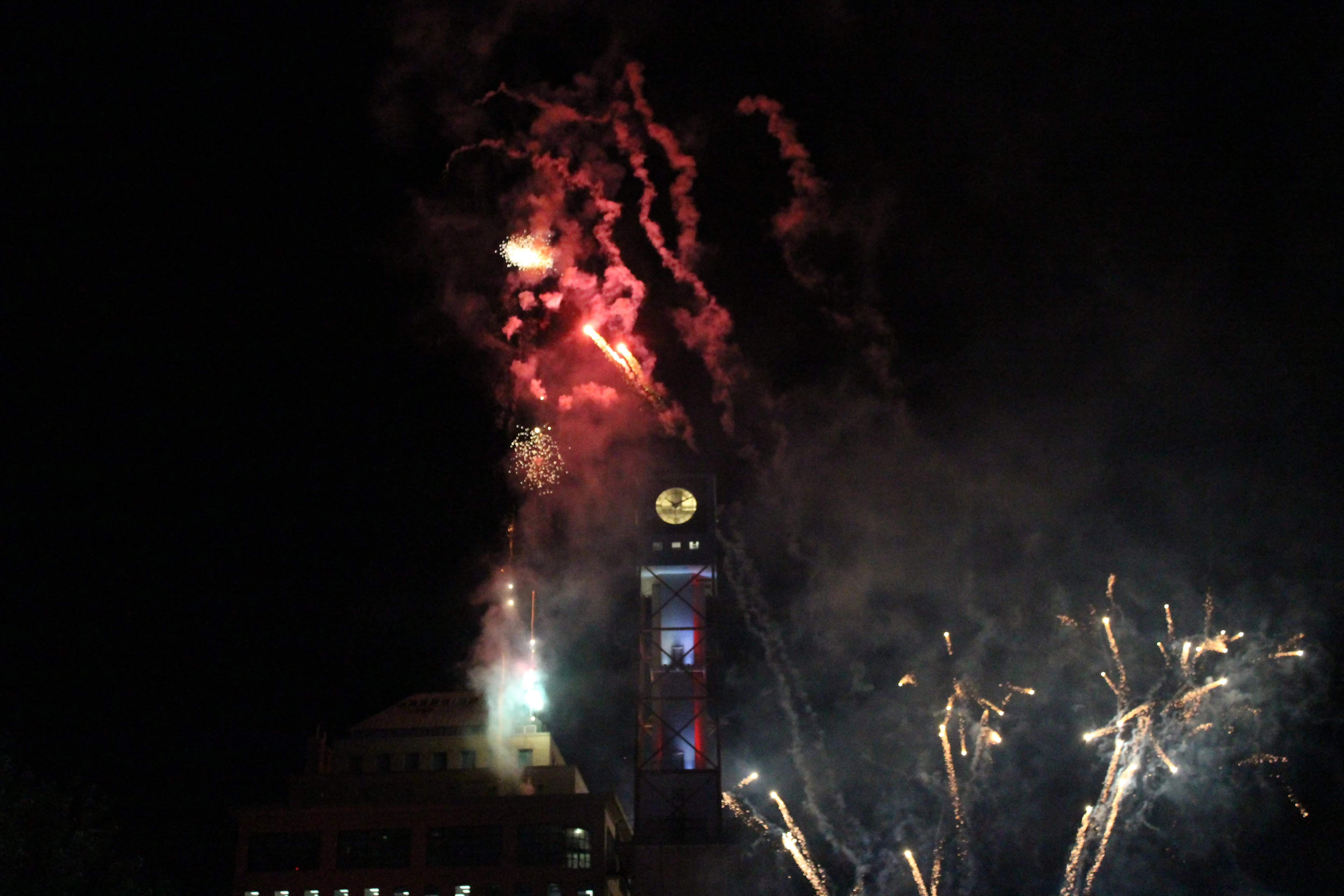 Red and gold fireworks bursting around a brick clock tower at night.