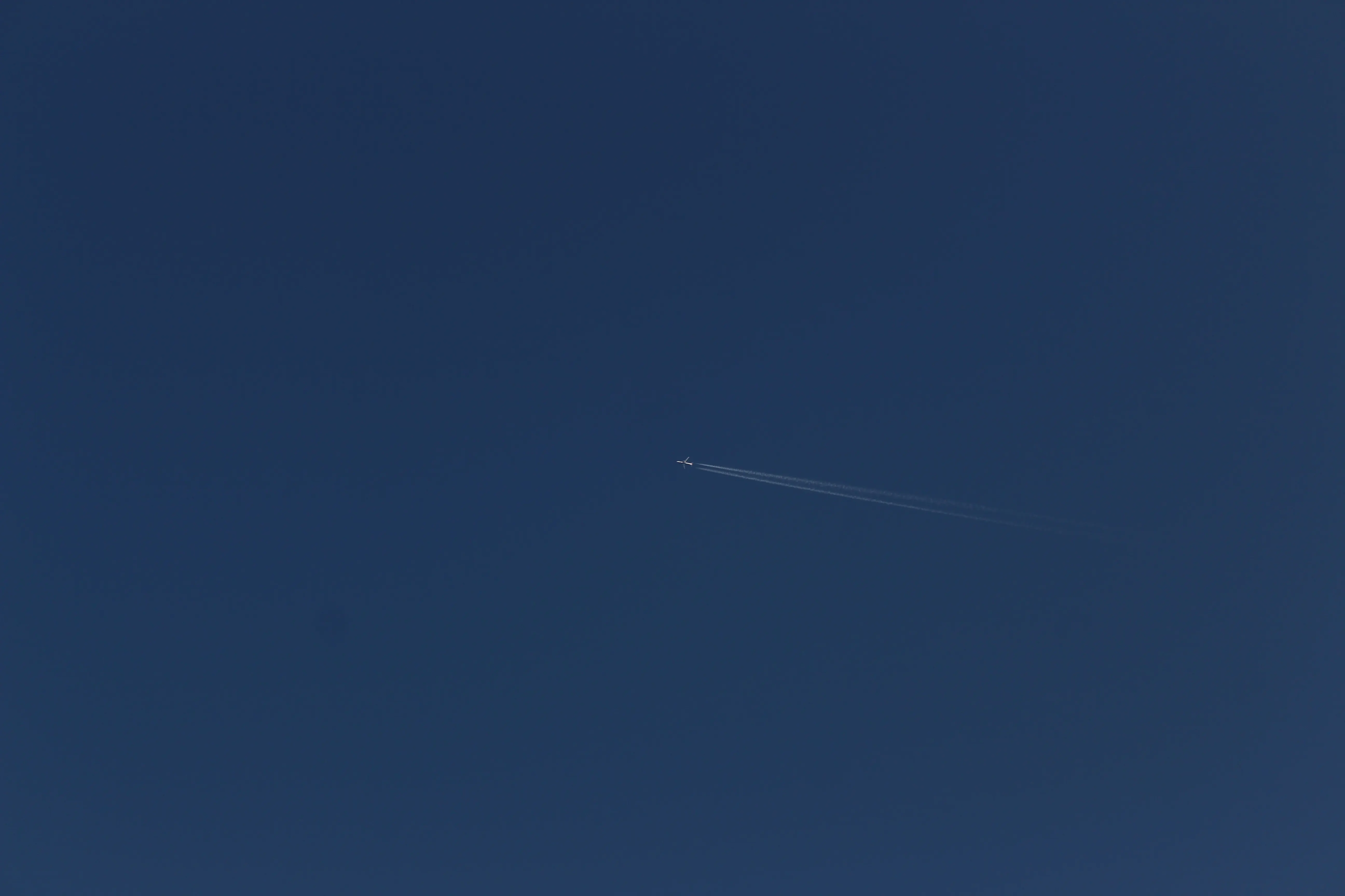 A jet airliner crossing a deep blue sky, leaving a long contrail diagonally across the frame.
