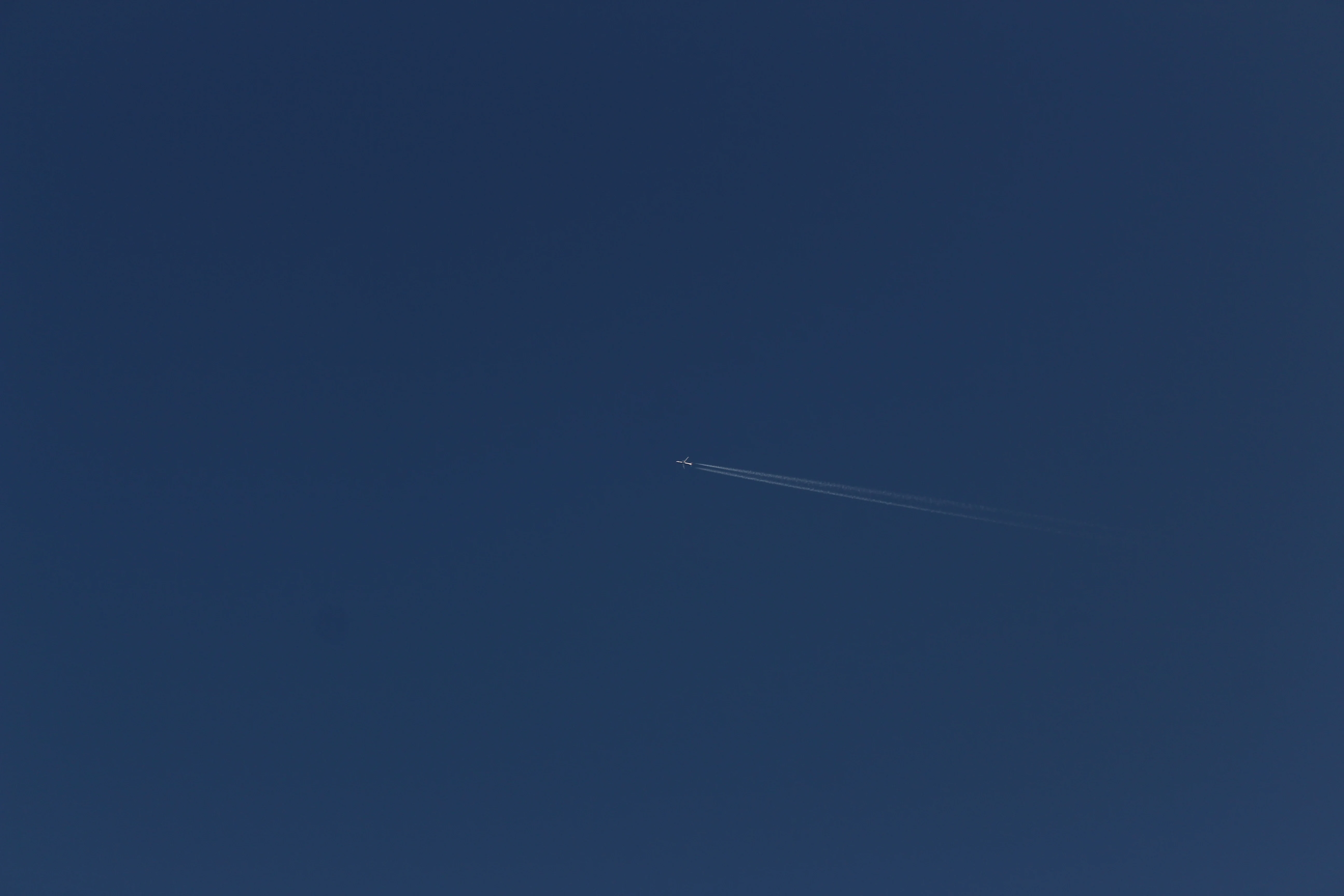 A jet airliner crossing a deep blue sky, leaving a long contrail diagonally across the frame.