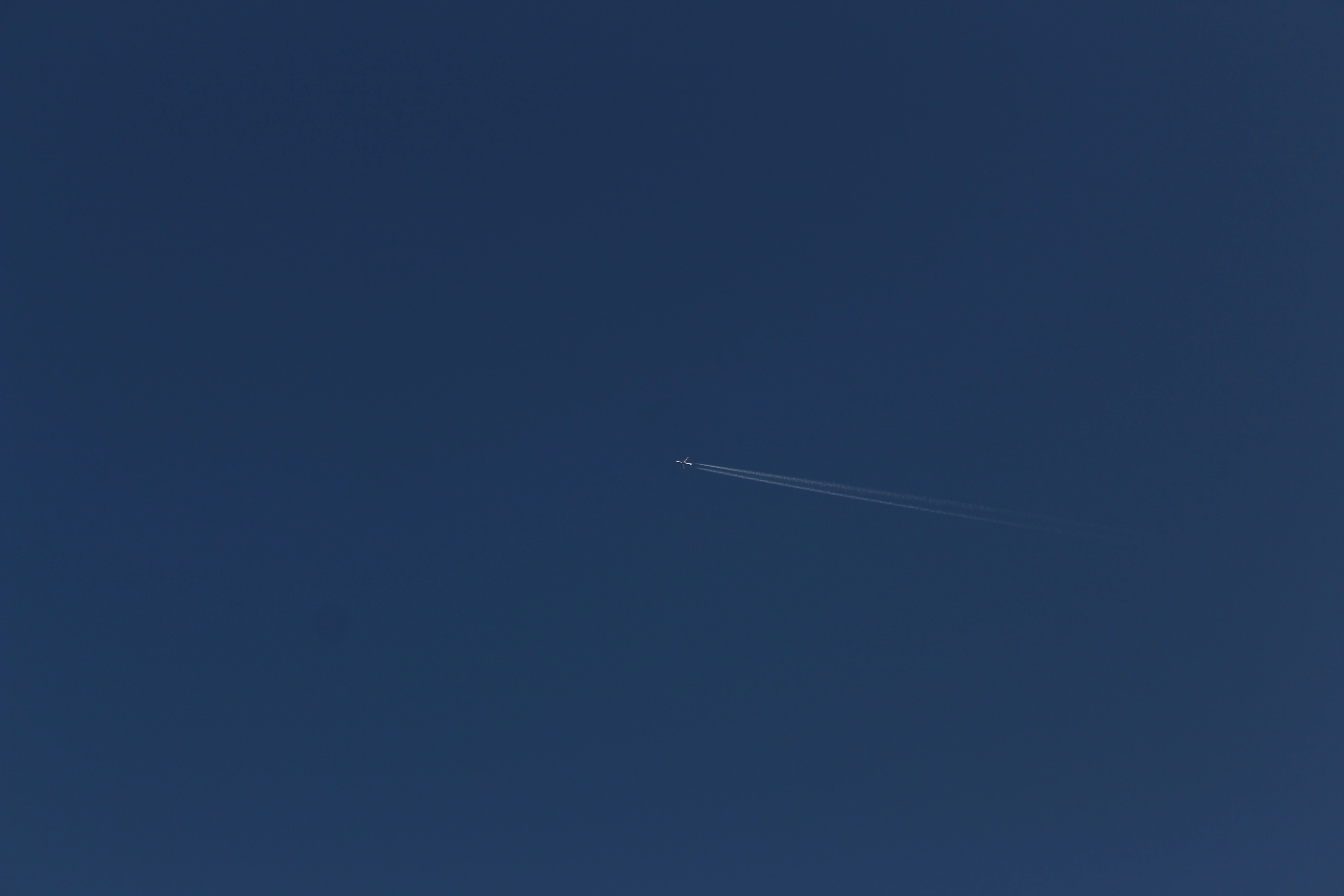 A jet airliner crossing a deep blue sky, leaving a long contrail diagonally across the frame.